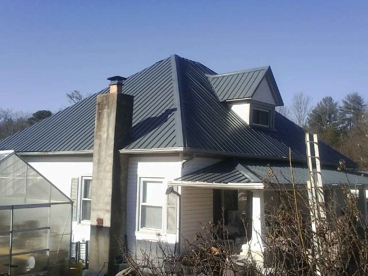 Dark blue standing seam metal roof on a white farmhouse with dormer — Slate & Tile Roof Repair by Roofing Brothers in Springwater