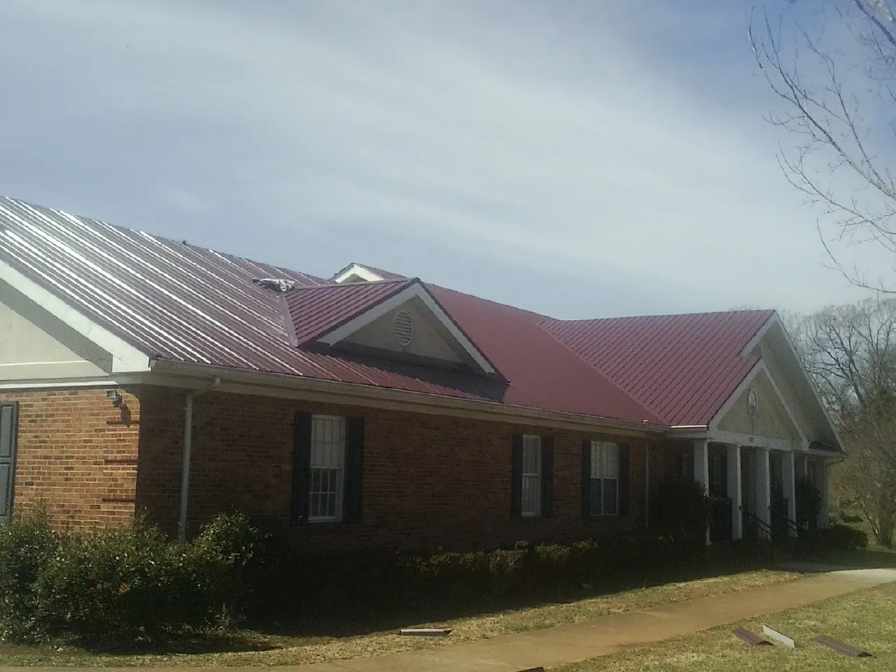 Red metal roof with gabled entries on a long brick building, from a Hail Damage Roof Repair job in Springwater