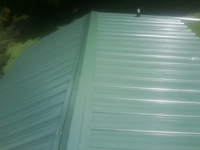 New green metal panels meeting at the ridge of a roof — Flat Roof Repair work by our crew in Springwater