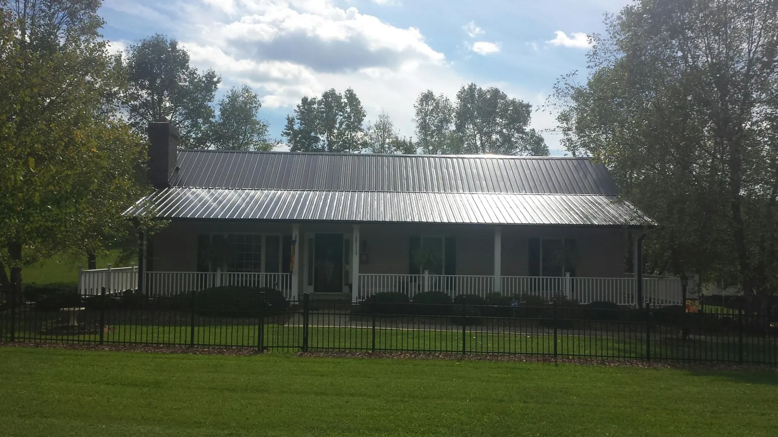 Gray metal roof on a brick ranch with a full width front porch — Gutter Guard Installation work by our crew in Springwater