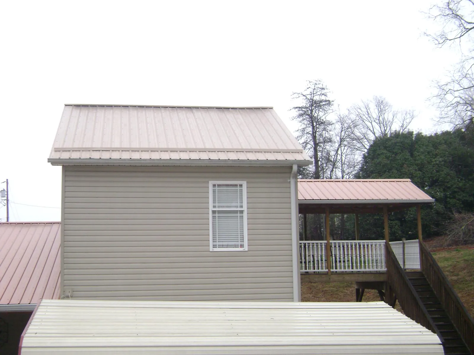 Tan metal roofs on a two story addition and attached porch, from a Roof Replacement job in Springwater
